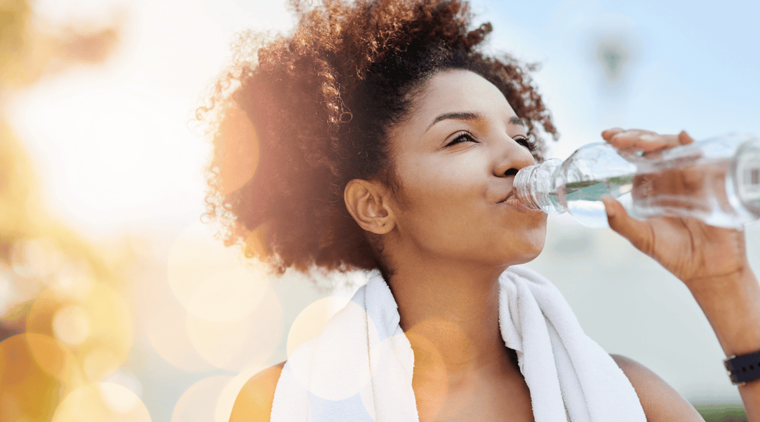 A woman drinking fresh water from her bottle for hydrated skin.