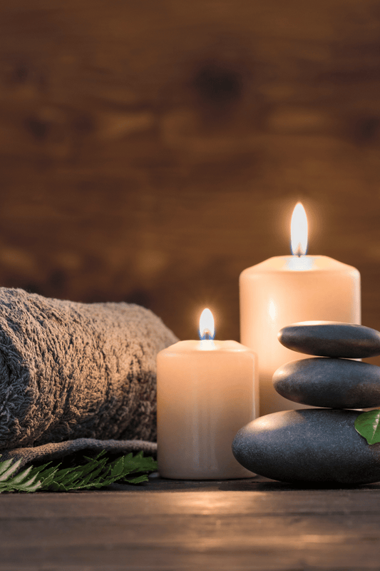 Spa environment, two lit candles, a warm towel roll and massage stones