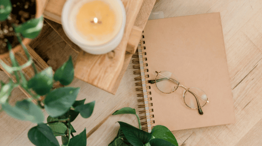 A burning candle with a journal and eye glasses