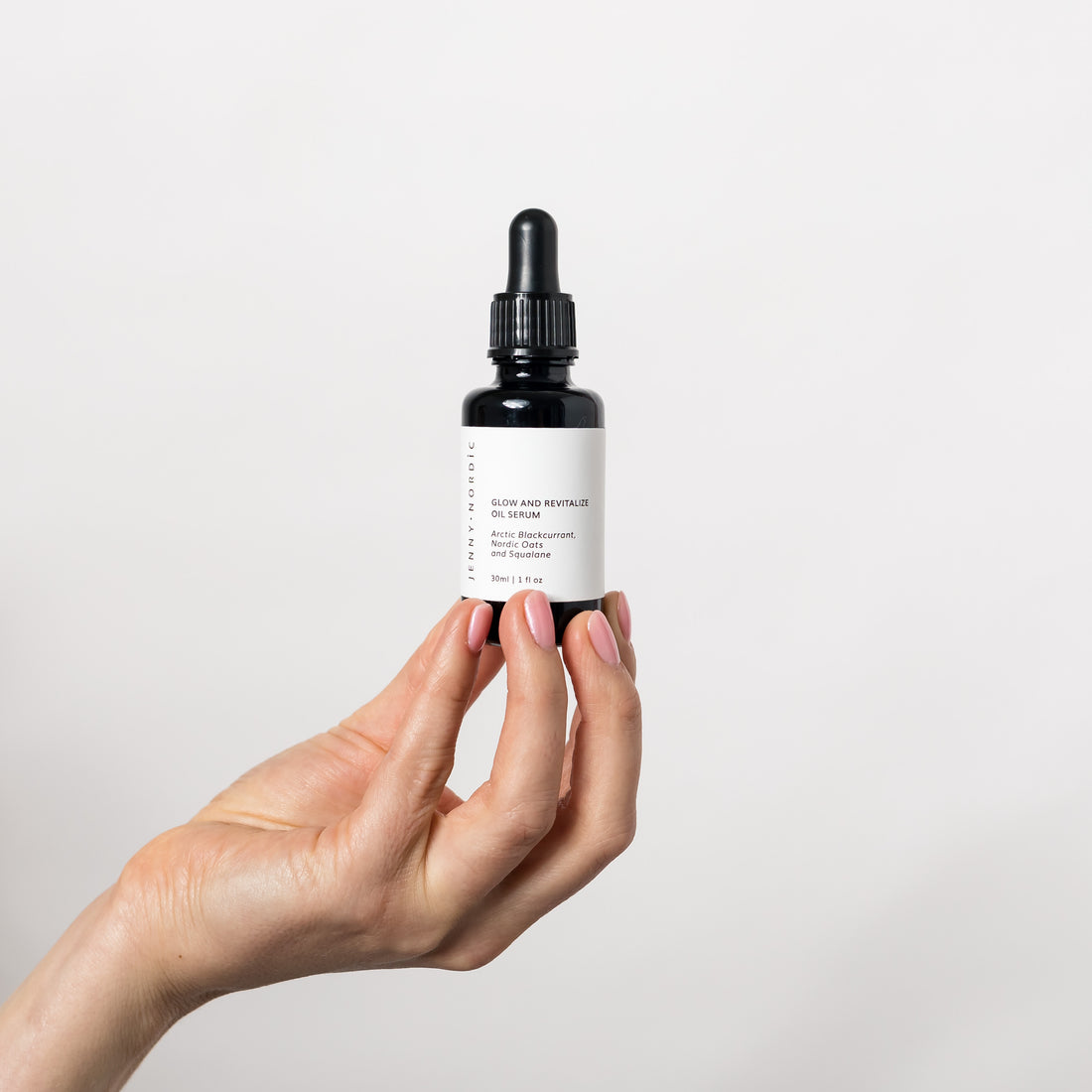 A hand holding Glow and Revitalize Oil Serum bottle.