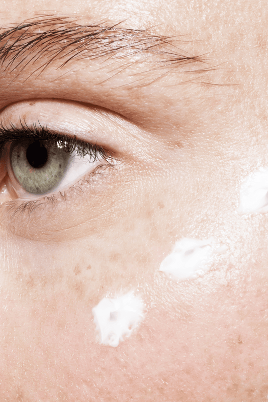 close up image of the corner of an eye, eyebrow visible and dots of face cream.