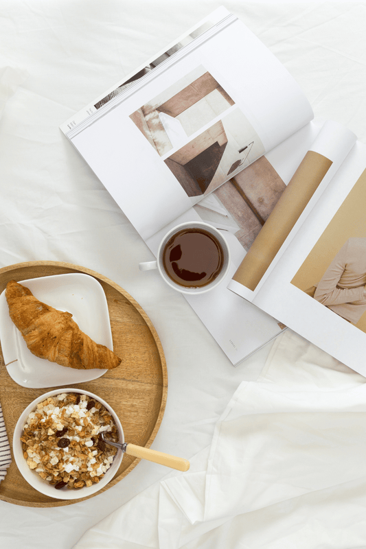 A calm and peaceful morning and breakfast set up with magazines and coffee on white sheets