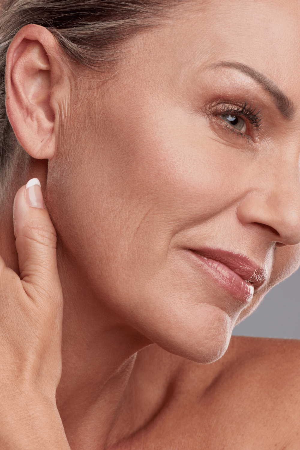 A close up sho of A white middle-aged woman watching into the distance, holding one hand on her neck.